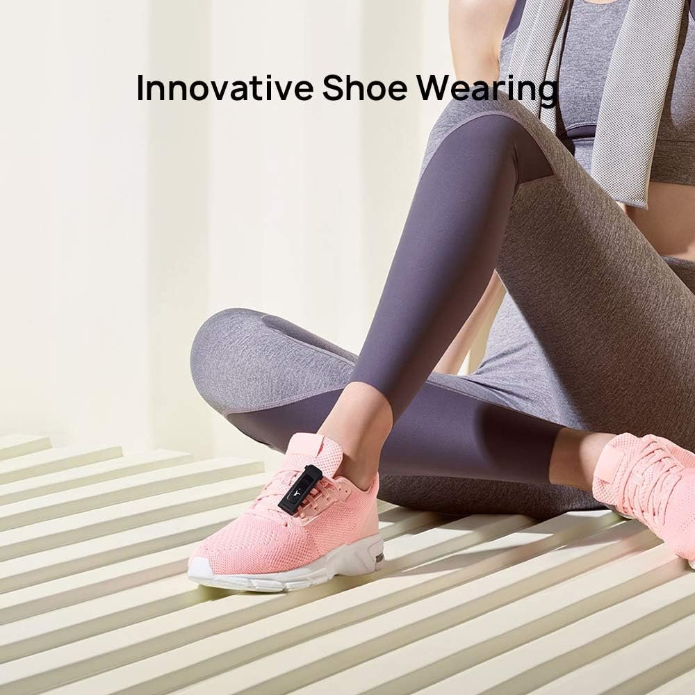 Mujer sentada en el suelo con mallas deportivas grises y zapatillas deportivas rosas, ajustándose una pulsera de fitness en su zapato, en un entorno interior luminoso con un fondo de líneas diagonales suaves.
